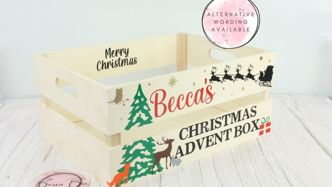 Wooden crate lettered “Becca’s Christmas Advent Box” with green trees, a deer and Santa’s sleigh