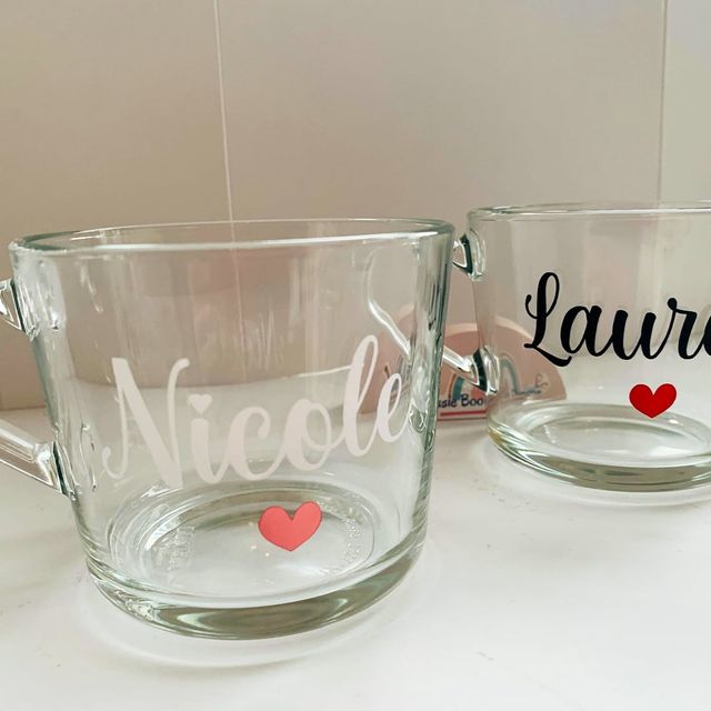 Two clear glass mugs, one with “Nicole” in white and one with “Lauren” in black, each with a small heart