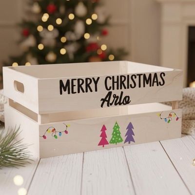 Wooden crate lettered “Merry Christmas Arlo” with pink, green and purple Christmas trees