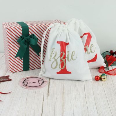 White drawstring bags with a red initial and a gold glitter name, “Izzie” and “Zac”