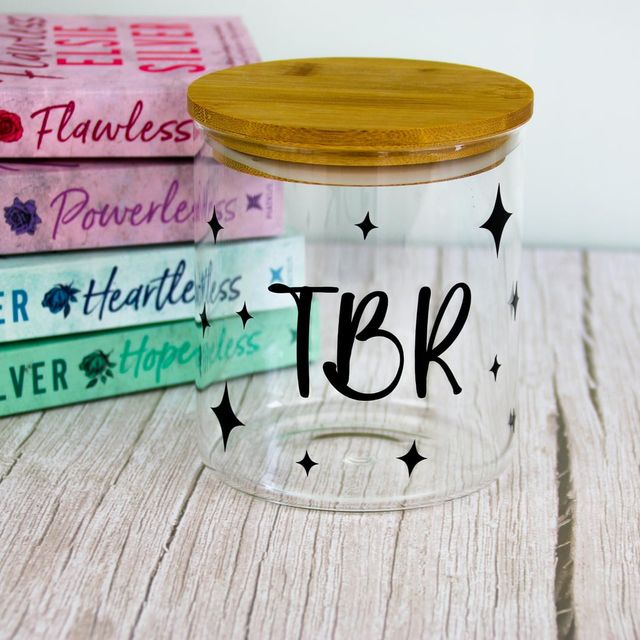 Glass jar with bamboo lid lettered “TBR” with stars, in front of a stack of books