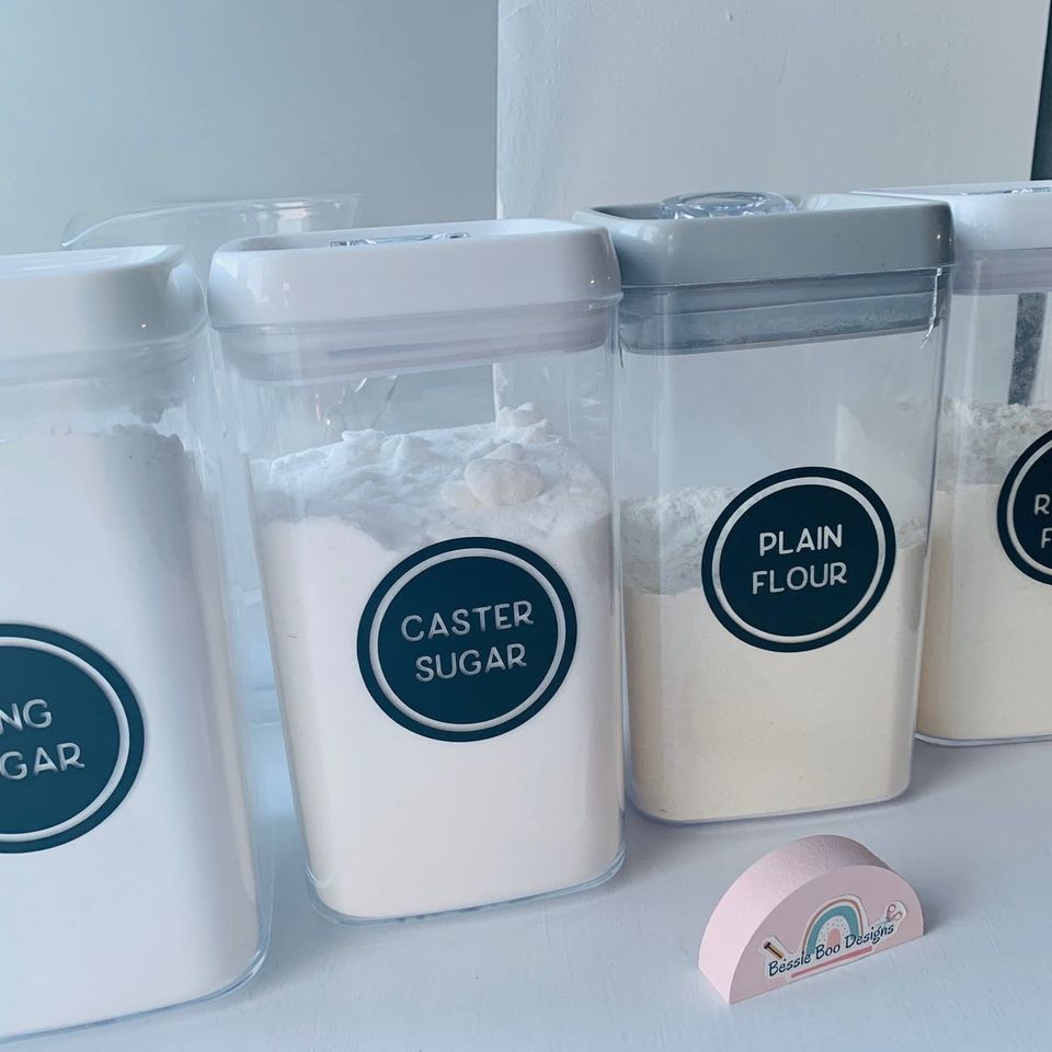 Storage containers with round navy labels reading “Caster sugar” and “Plain flour”
