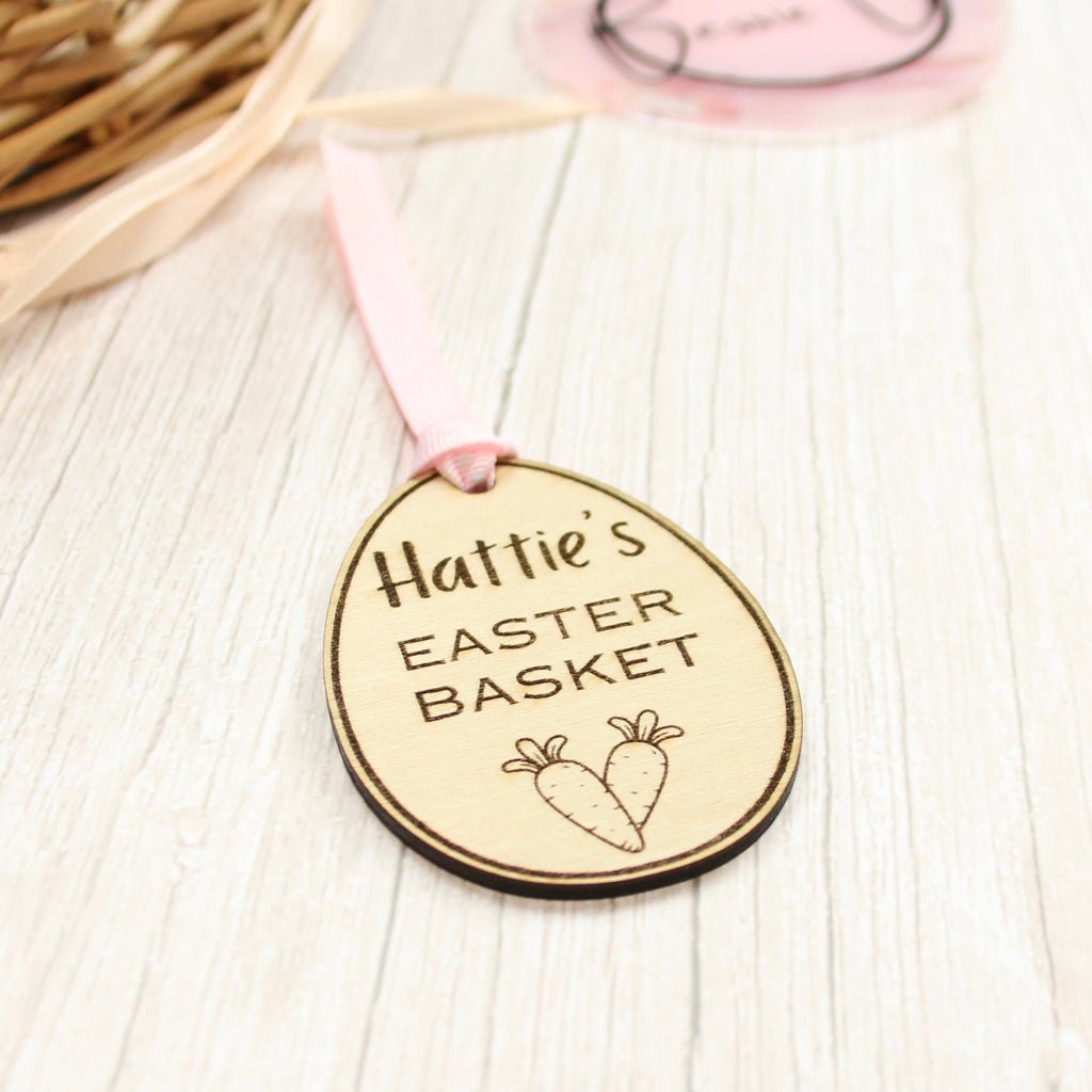 Easter basket wooden tag to be used as an Easter Decoration. Tag is in the shape of an Easter egg and is made from 3mm Plywood. includes personalised text, e.g. name of a child. The tag says: Hattie&#39;s Easter Basket. It includes 2 small carrots.